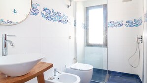 Un baño con lavamanos blanco, bidé, inodoro, un espejo y cabina de ducha con mampara de vidrio.