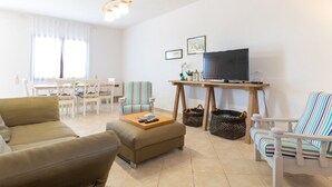 Una sala de estar con sofá, reposapiés, sillones a rayas, televisor, mesa de madera y comedor con sillas.