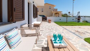 Un patio con mobiliario exterior, una mesa con vasos y un edificio con tejado de tejas al fondo.