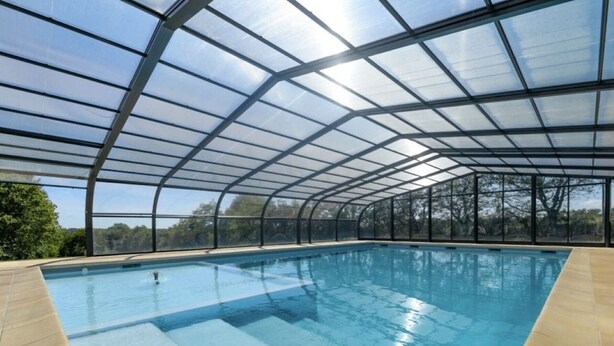 Una piscina interna con tetto in vetro e pareti trasparenti, circondata da un pavimento e pareti color beige.