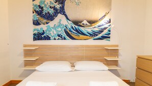 A hotel room with a bed, pillows, a wooden headboard, a wall-mounted artwork, and a wooden dresser.