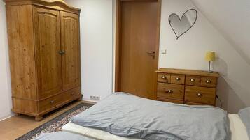 Un dormitorio con cama, armario de madera, cómoda, espejo y puerta.