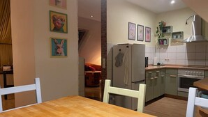 A modern kitchen with a wooden dining table, white chairs, and a refrigerator. - Vacation apartment with family bed - ideal for families, groups and fitters (Groß Niendorf)