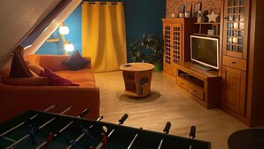 A cozy living room with a sofa, a television, a wooden cabinet, and a foosball table. - Vacation apartment with family bed - ideal for families, groups and fitters (Groß Niendorf)