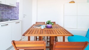 A compact kitchen with white cabinets, a wooden table, and a blue chair. - Casa Tatti- Calm&Natural (San Giovanni di Sinis)