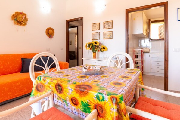 A dining area with a table covered in a sunflower tablecloth, a sofa, and chairs.
