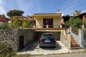 A two-story house with a car parked in the driveway, stone walls, and a wooden pergola.