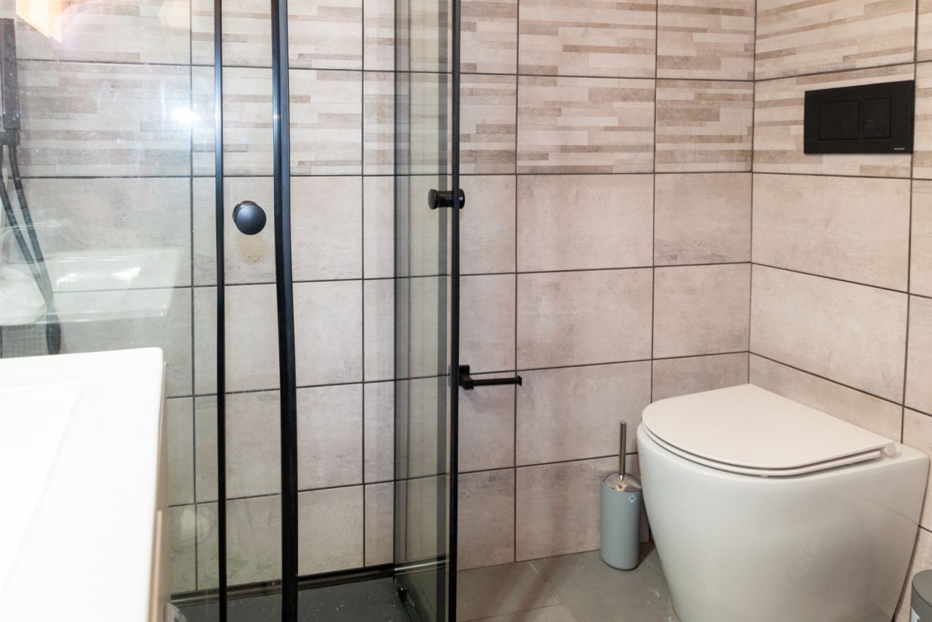 Une salle de bain avec une douche à parois en verre, des toilettes et une poubelle.
