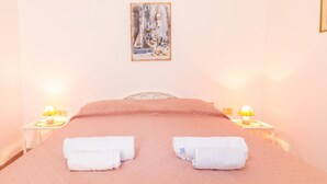 Una cama bien hecha con dos toallas, un cuadro en la pared y lámparas de noche.