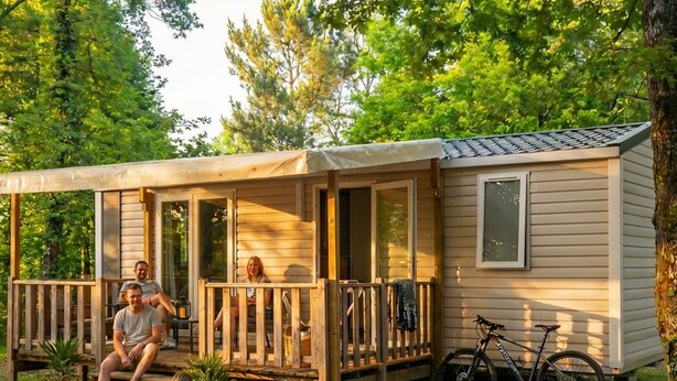 A small wooden cabin with a porch, a bicycle, and a basketball. - Cozy mobile home with terrace - Sleeps 6 (Saint-Gérons)
