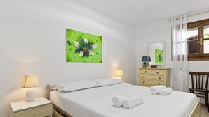 A hotel room with a bed, two bedside tables, a nightstand, a dresser, a chair, and a window with curtains. - Casa S'Architteddu- Coastal Escape (San Vero Milis)