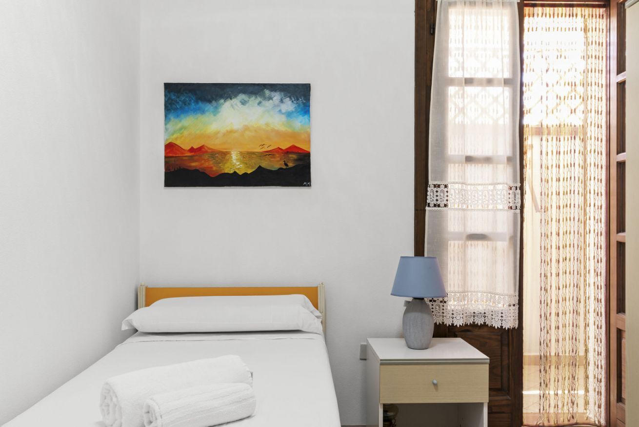 A hotel room with a bed, a nightstand with a lamp, a painting on the wall, and a window with curtains.