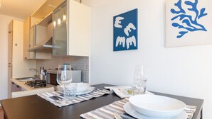 Een eethoek met een tafel voor twee personen, een keuken op de achtergrond en twee abstracte kunstwerken aan de muur.