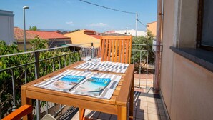 Een houten tafel met tijdschriften en glazen op een balkon met uitzicht op gebouwen en een heldere lucht.
