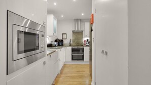 A modern kitchen with stainless steel appliances, white cabinetry, and a wooden floor. - Old Farm- North East Escapes (Bamburgh)