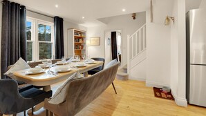 A dining area with a wooden table set for four, surrounded by upholstered chairs. A bookshelf and a framed picture are visible in the background. - Old Farm- North East Escapes (Bamburgh)