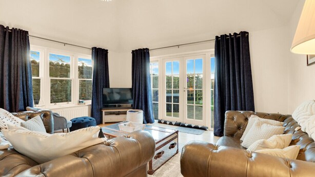 A spacious living room with leather sofas, a flat-screen TV, and large windows with curtains. - Old Farm- North East Escapes (Bamburgh)