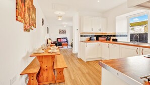 A modern kitchen with white cabinets, a wooden dining table, and a view of the outside. - Cheviot - North East Escapes (Wooler)