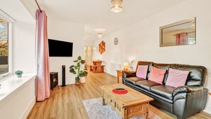 A modern living room with a leather sofa, wooden coffee table, and a large window with curtains. - Cheviot - North East Escapes (Wooler)