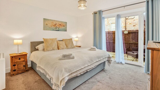 A bedroom with a bed, bedside lamps, a painting, and a view of the outside. - Cheviot - North East Escapes (Wooler)