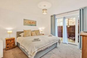 Ein Schlafzimmer mit einem Bett, Nachttischlampen, einem Gemälde und Blick ins Freie.