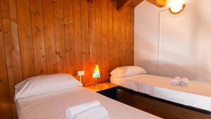 Een kamer met twee bedden, houten wanden, een nachtkastje met lamp en een wandlamp.