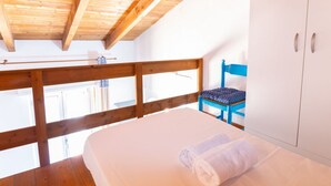 Een slaapkamer met een houten plafond, een bed met witte lakens, een blauwe stoel en een witte kledingkast.