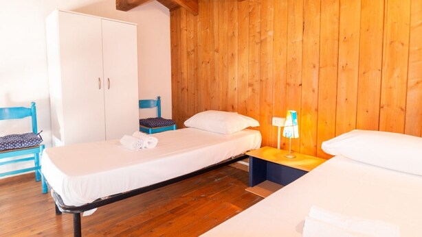 Une pièce aux murs lambrés, comprenant un lit, une armoire, une chaise et une table de chevet avec une lampe.