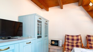 Een kleine kitchenette met een televisie, een magnetron en een kastje. Er staan twee ruitjesstoelen en een tafel met een tafelkleed.