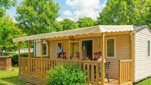 Een klein houten huisje met een veranda, meerdere ramen en een overdekt terras.