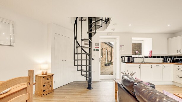 Eine moderne Küche mit weißen Schränken, einer schwarzen Wendeltreppe und einer hölzernen Bank.