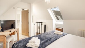 Ein Schlafzimmer mit einem großen Bett, einem Schreibtisch mit Fernseher, einer Holztür, einer Heizung und einem Oberlicht.