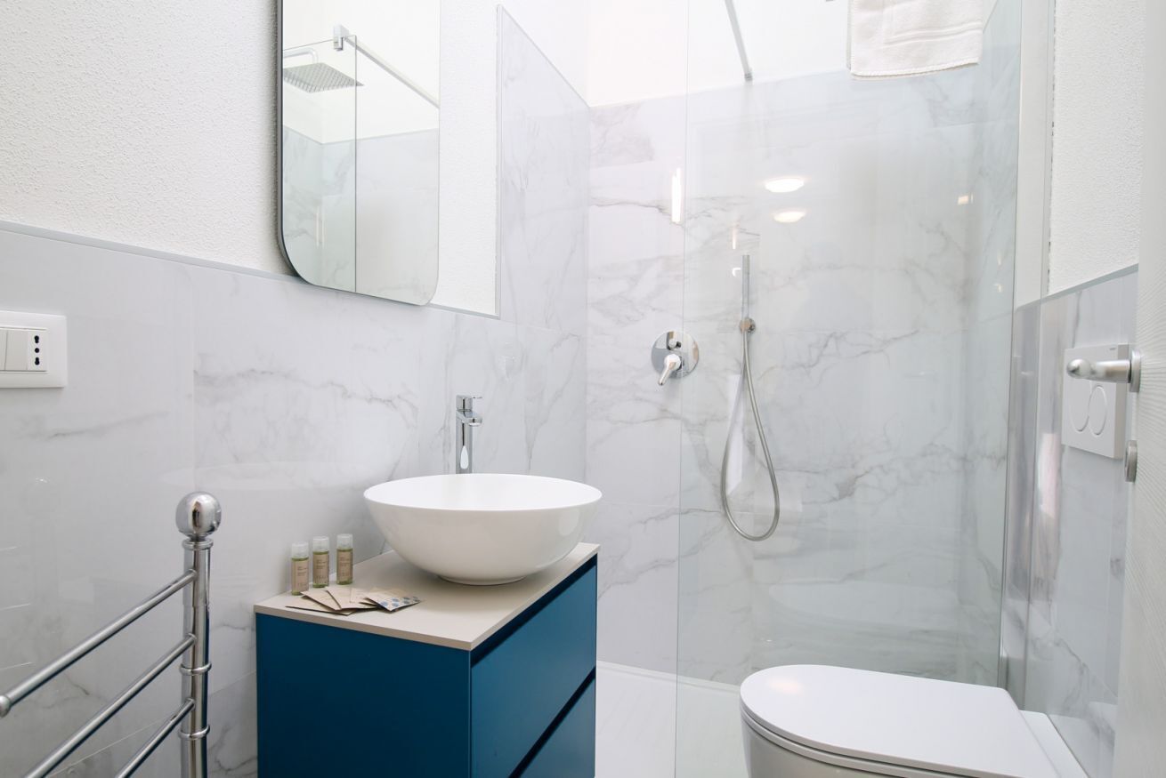 A modern bathroom with a white sink, blue cabinet, and a glass shower enclosure.