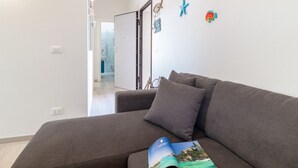 Ein graues Sofa mit einer Zeitschrift, eine weiße Tür und ein Flur, der zu einem Badezimmer führt.