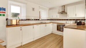 Una cocina moderna con armarios blancos, encimera de madera y horno empotrado.