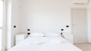 Minimalistiseen tyyliin sisustettu hotellihuone, jossa on suuri sänky, yöpöydät, vaatekaappi ja ilmastointilaite.