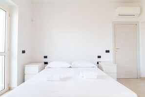 Habitación de hotel minimalista con una cama grande, mesitas de noche, un armario y un equipo de aire acondicionado.