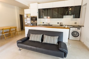 Un appartement moderne comprenant un canapé, une table à manger, une cuisine avec un lave-linge et une grande fenêtre.