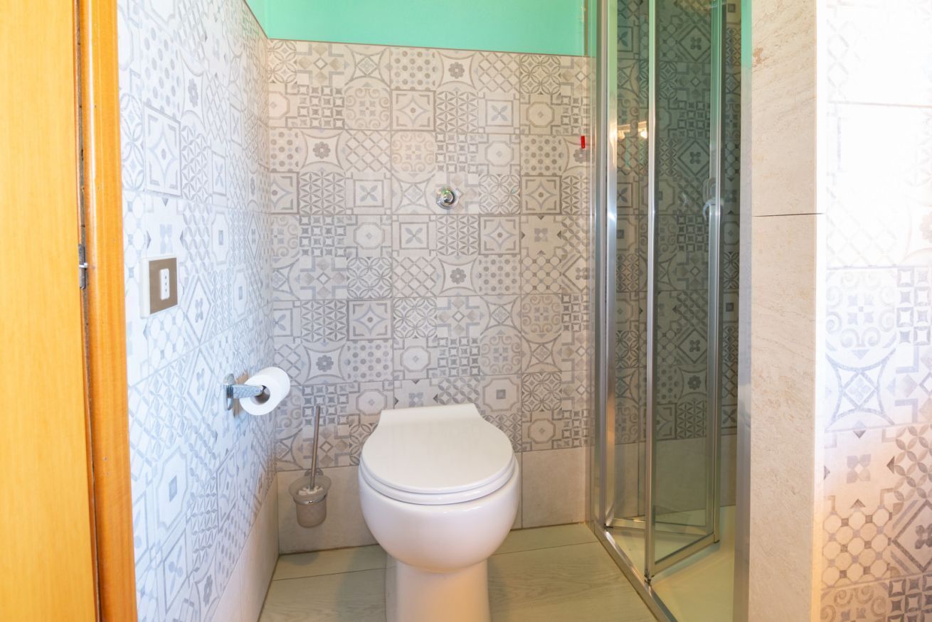 Een badkamer met patroon betegelde vloer, toilet, glazen douchecabine en een houten deur.