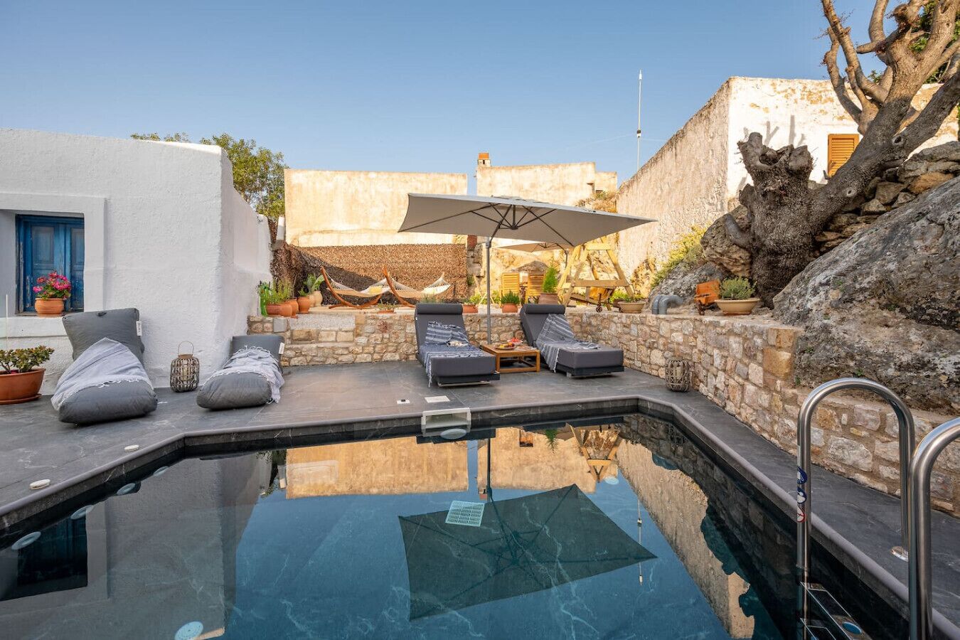 A swimming pool with lounge chairs and an umbrella, surrounded by stone walls and potted plants.
