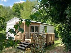 Ein kleines, eingeschossiges Mobilheim mit einer Holzterrasse und einer Veranda.
