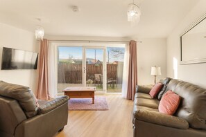 A spacious living room with two leather sofas, a wooden coffee table, and a television mounted on the wall. - Hethpool North East Escapes (Wooler)