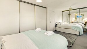 Moderni hotellihuone, jossa on suuri sänky, pienempi sänky, peili ja kattovalaisin.