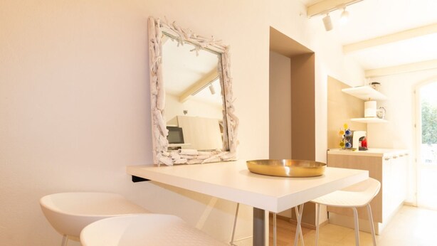A modern kitchen with a white countertop, two white bar stools, a gold bowl, and a mirror with a unique frame.
