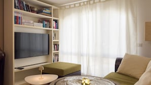 A living room with a flat-screen TV, bookshelves, a green sofa, a small round table, and a wooden coffee table.