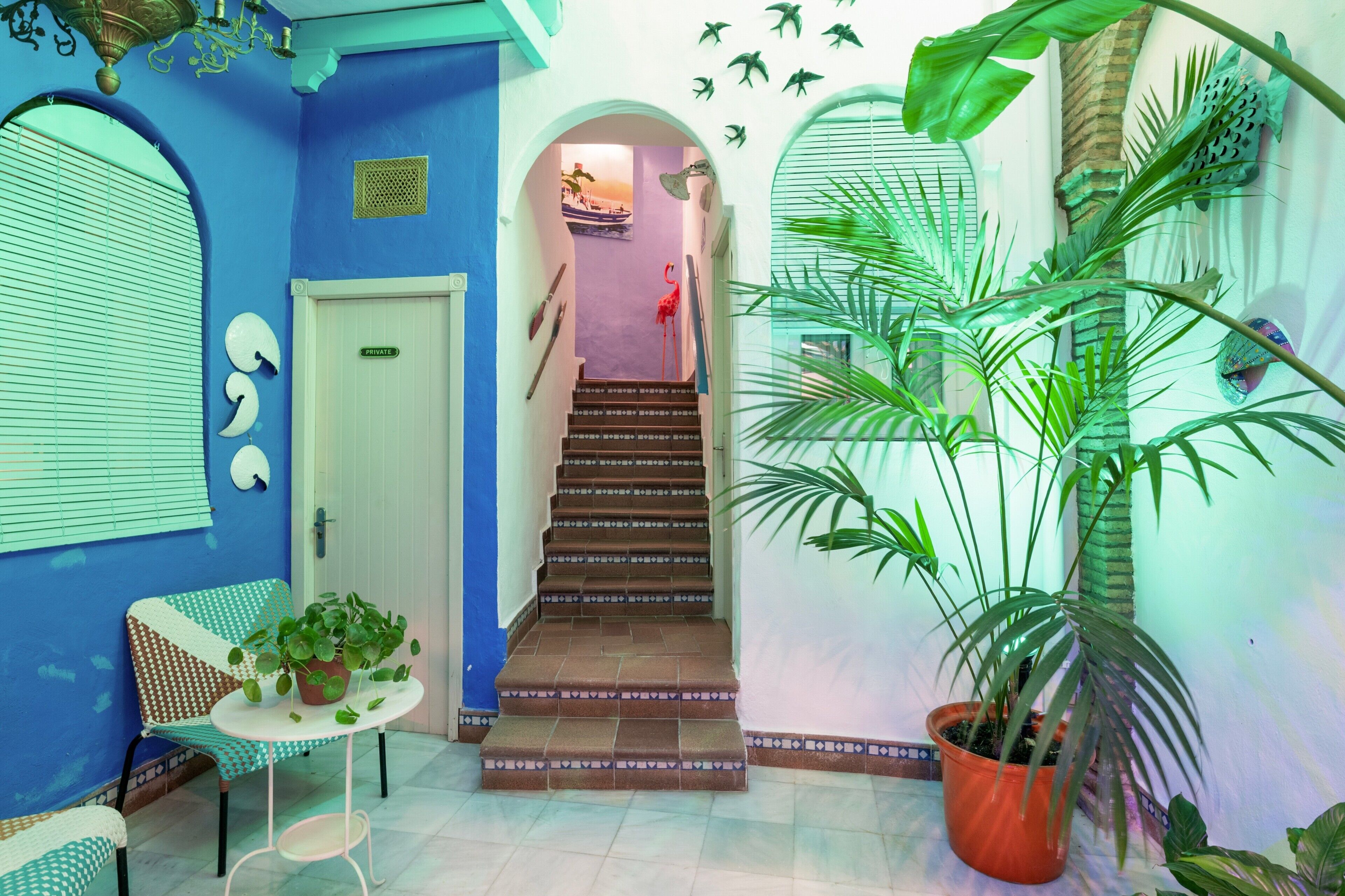 A staircase leading to a second floor, a white door labeled 'PRIVATE,' a small round table with a plant, and a chair with a patterned cushion.