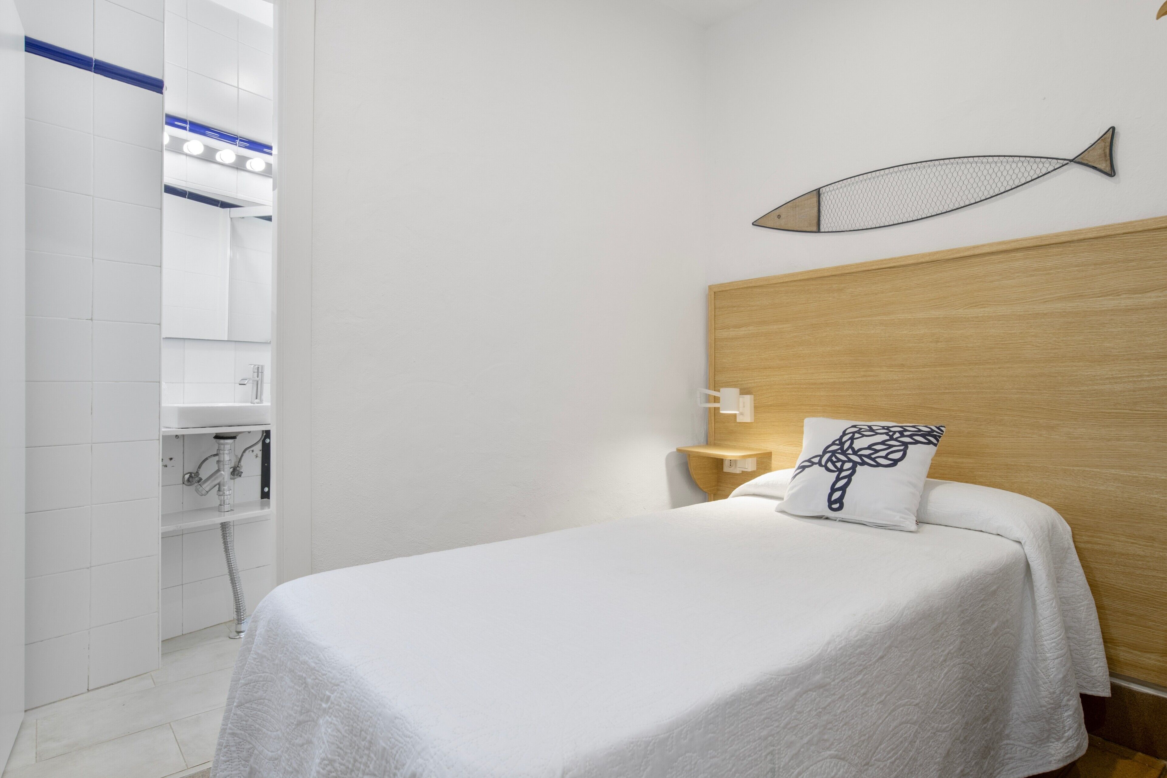 Une chambre d’hôtel avec un lit, une tête de lit en bois, une décoration murale représentant des poissons et une salle de bain blanche visible à travers une porte ouverte.