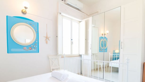 Een slaapkamer met een bed, een spiegel, een zeester decoratie en een deur die uitkomt op een balkon.
