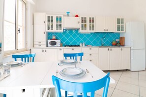 A kitchen with white cabinets, a blue tiled backsplash, a white table with blue chairs, and a window. - Casa dei Catalani-Rustic Charm (Torre Grande)