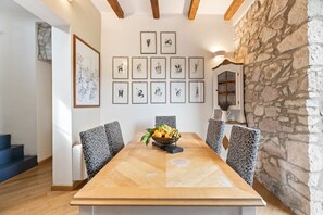 A dining area with a wooden table, patterned chairs, a stone wall, and framed artwork on the wall. - Bosa Eye House 1873 | Borgo (Bosa)